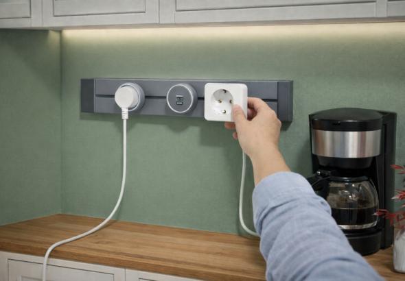 Persona instalando un enchufe modular en una cocina con pared verde y encimera de madera, sin necesidad de obras