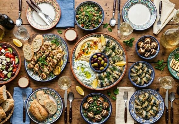 Imagen que muestra una mesa con platos de comida de dieta mediterránea con pollo, pescado, verduras, ensalada, pan, aceite de oliva