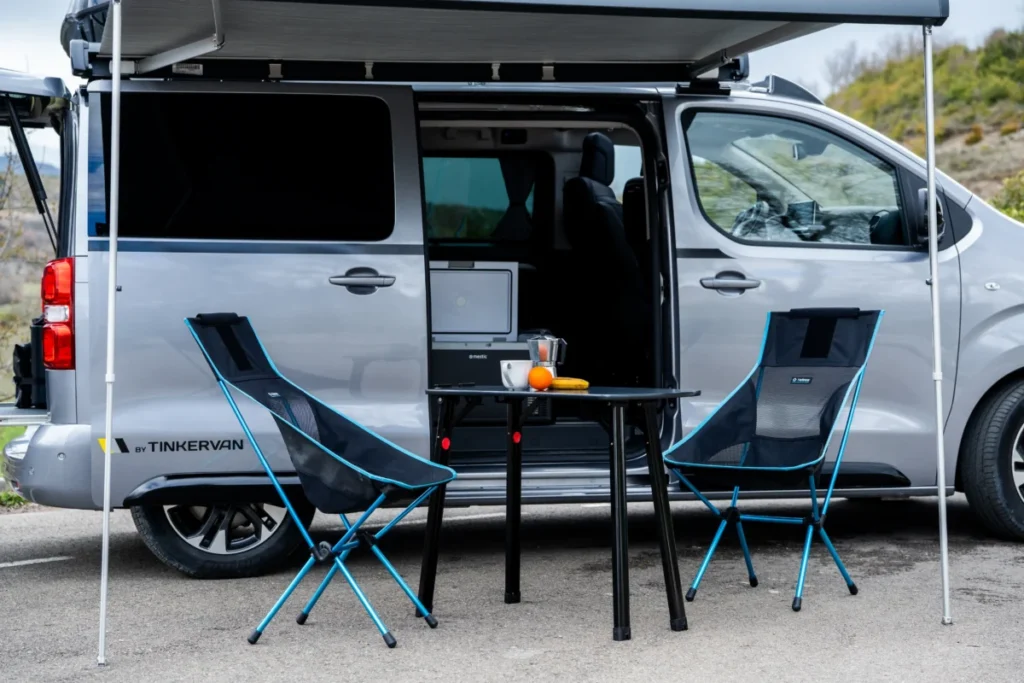 ¿Tu casa o tu coche? La libertad total del nuevo Opel Zafira de Tinkervan Imagen exterior del nuevo Opel Zafira de 2026 con el toldo extendido y la mesa y sillas debajo de este