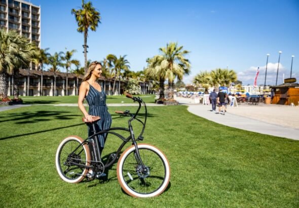 Imagen que muestra a una chica con sandalias en verano sosteniendo una bici sobre el césped verde