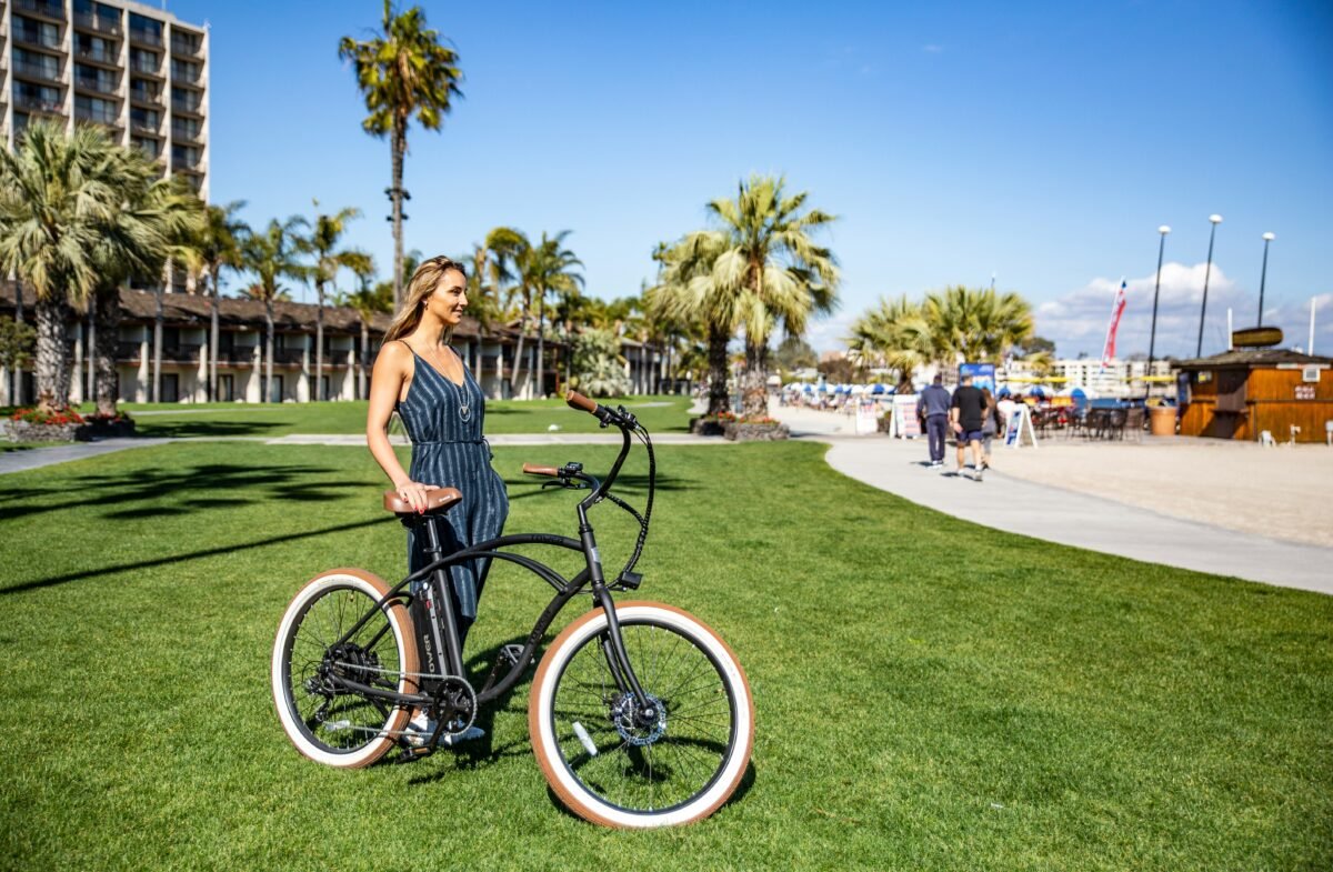 Del chollo de Sfera al lujo de Timberland: las sandalías de cuña del verano Imagen que muestra a una chica con sandalias en verano sosteniendo una bici sobre el césped verde