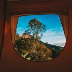 Imagen del interior de una tienda de campaña con vistas por la ventana a una montaña en un festival