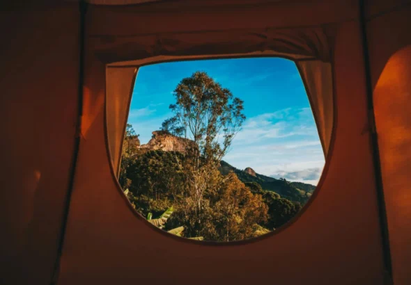 Imagen del interior de una tienda de campaña con vistas por la ventana a una montaña en un festival