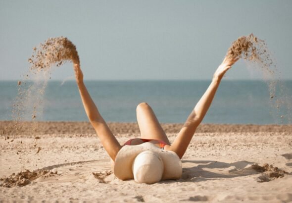 Imagen que muestra a una chica en la arena de la playa tumbada con uno de los bañadores tendencia de verano