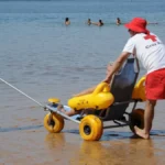 Imagen que muestra a dos técnicos en la playa de Valencia atendiendo a una persona con necesidad de baño adaptado
