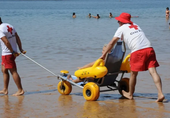 Imagen que muestra a dos técnicos en la playa de Valencia atendiendo a una persona con necesidad de baño adaptado