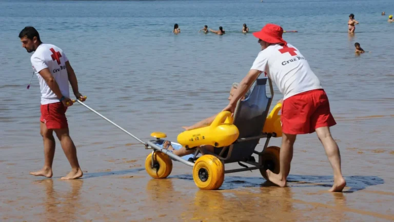 Imagen que muestra a dos técnicos en la playa de Valencia atendiendo a una persona con necesidad de baño adaptado