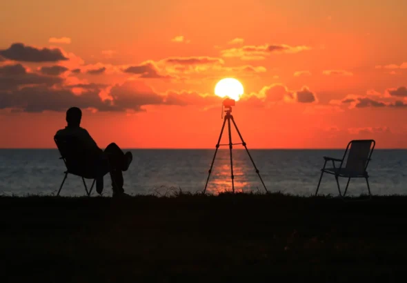 Imagen que muestra un eclipse solar y una persona sentada en la playa observando