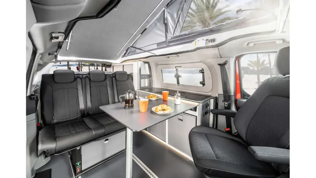 Ni hotel ni apartamento: la tendencia que arrasa para viajar por Andalucía este verano Imagen que muestra el interior de la autocaravana karman duncan 500 con asientos delanteros girados , enfrentados a los asientos traseros con una mesa de comedor en medio.