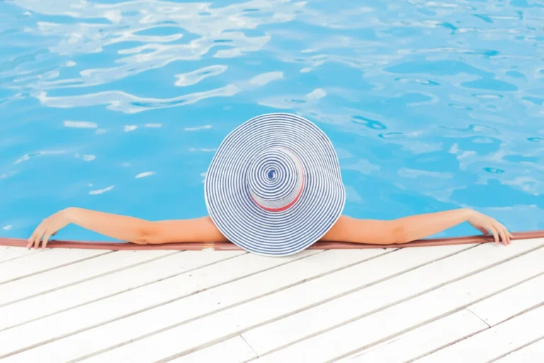 Flamingueo pone de moda la playa con sus accesorios de color rosa. Toallas, flotadores, sombrillas... la imagen muestra a una chica en una piscina con un gorro preparando sus complementos de Flamingueo
