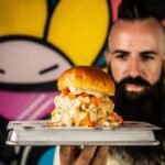 Moflete, el restaurante de Joe Burger Challenge , tiene un descuento hasta final de septiembre en sus menús para 2 y 4 personas. En la imagen muestra a Joe Burger con una hamburguesa de Moflete en la mano.