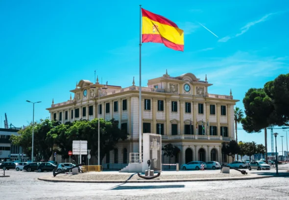 La regularización extraordinaria se ilustra con un edificio en España y su bandera. Imagen de recurso.