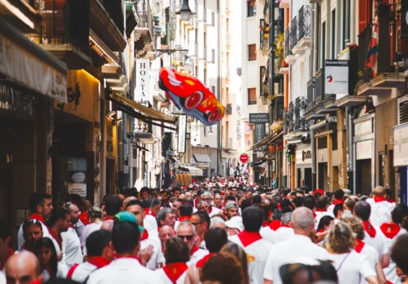 San Fermín , donde muestra una calle llena de gente con la tradicional vestimenta de blanco con pañuelo rojo.