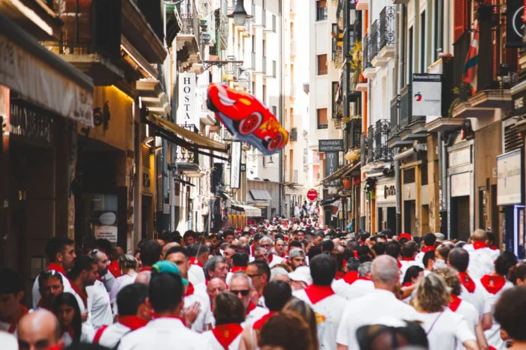 San Fermín , donde muestra una calle llena de gente con la tradicional vestimenta de blanco con pañuelo rojo.