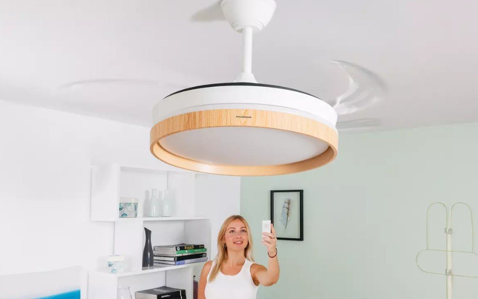 Las aspas de este ventilador de techo se esconden cuando lo apagas Imagen que muestra el ventilador de techo de color blanco con acabados en madera y las aspas desplegadas.