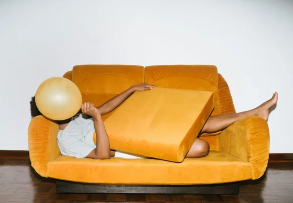 Imagen que muestra una persona agobiada por el precio del alquiler en un sofá amarillo tumbada con la cara tapada
