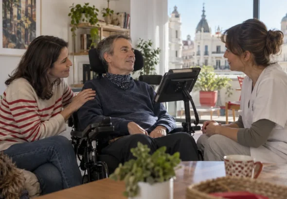 Ayudas ELA en Madrid: persona con ELA acompañada por una familiar y una profesional sanitaria